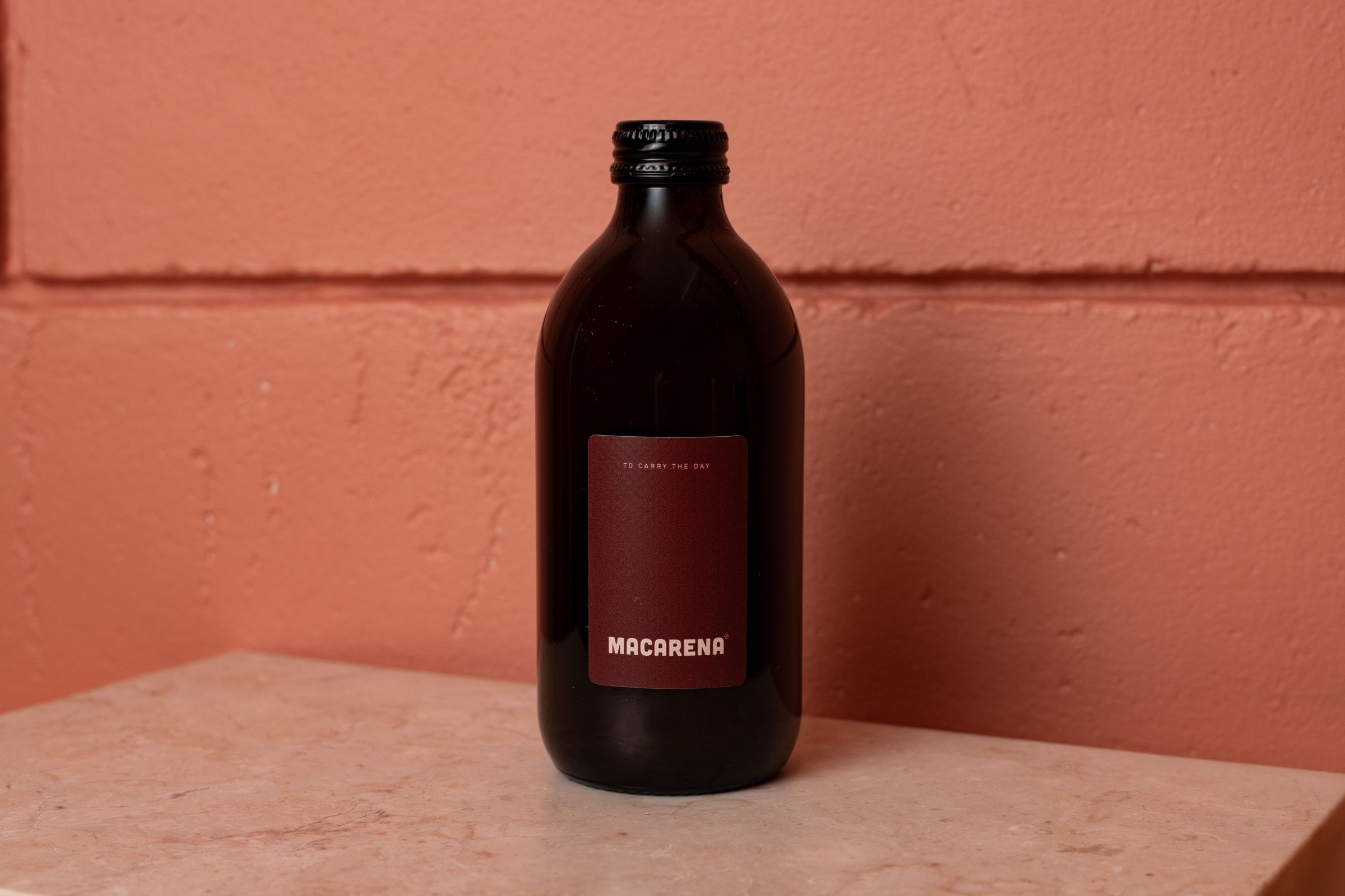 A bottle of Macarena on a marble block against a terracotta wall