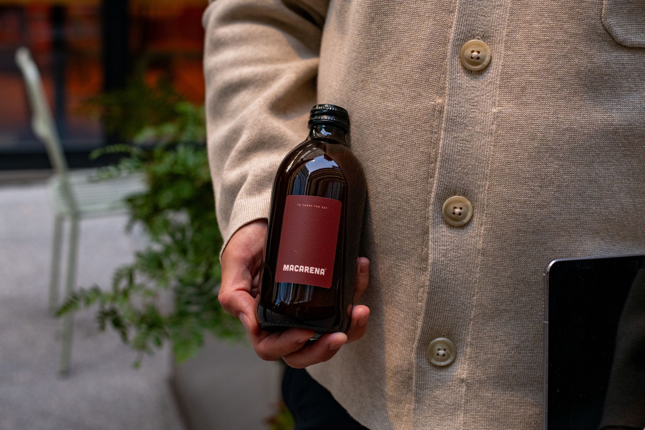 A bottle of Macarena concentrate held in one hand, a tablet in the other